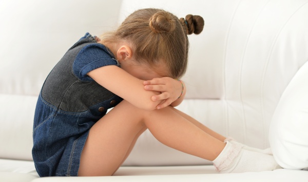 Mädchen sitzt wegen Vitamin D Mangel müde mit dem Kopf auf den Knien am Sofa