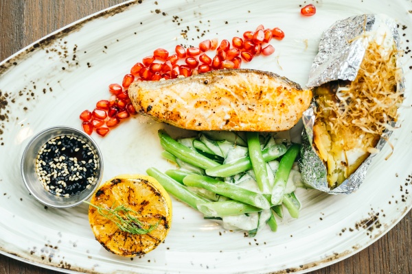 Auf einem Teller liegen Fisch und Gemüse. Sie enthalten die richtigen Nährstoffe, um einen Muskelkater vorzubeugen.