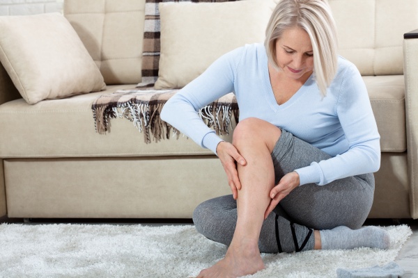 Am Boden sitzende Frau hält ihr durch Arthritis schmerzendes Bein
